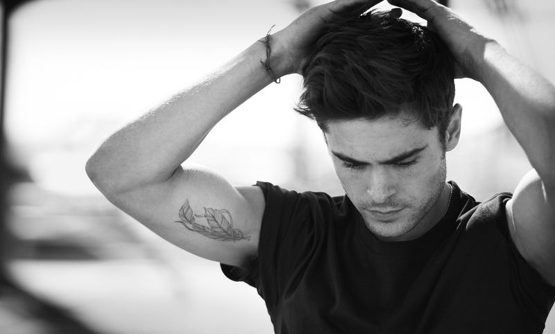 Zac Efron raising his arm with the feather tattoo visible