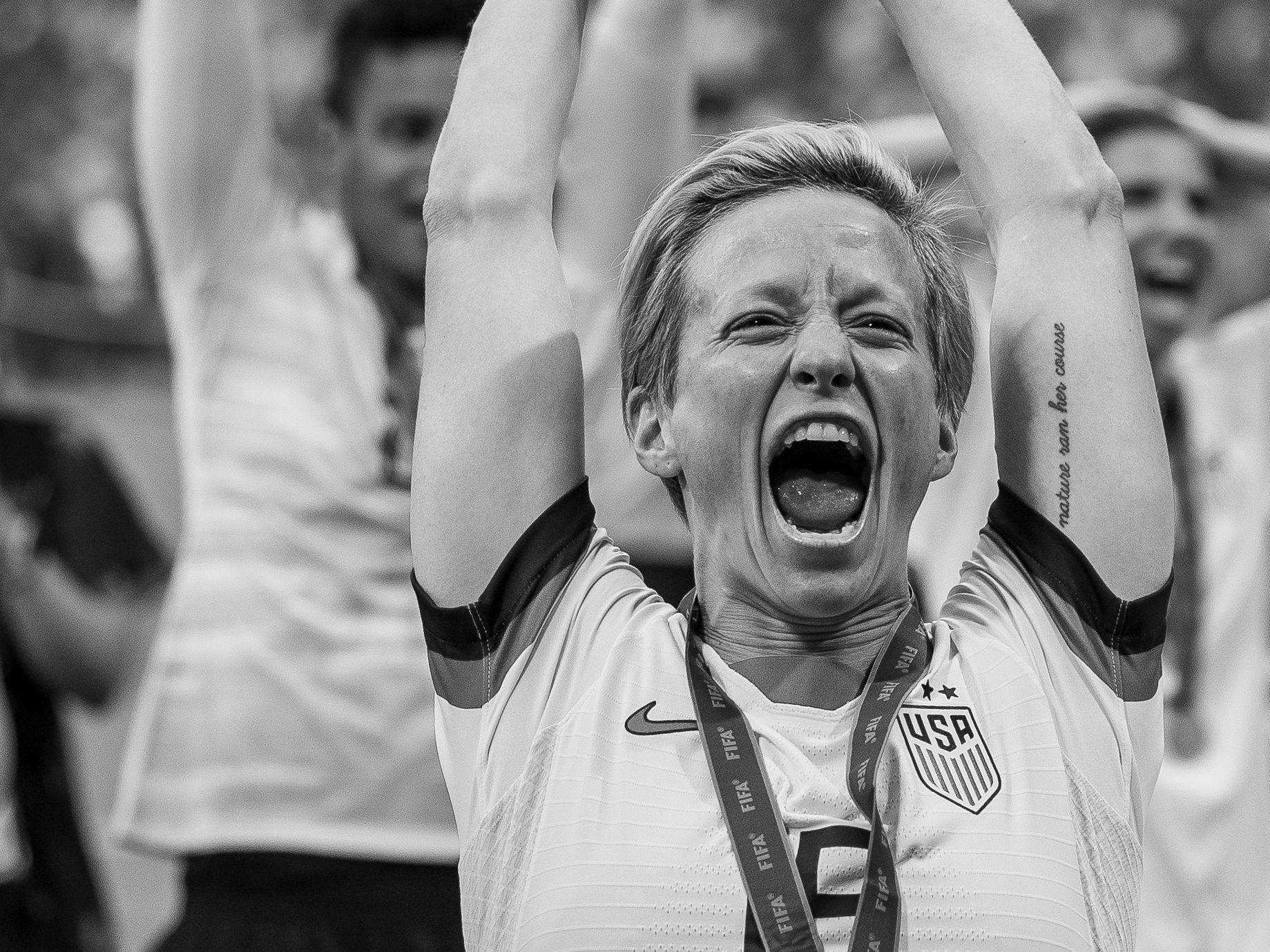 Megan Rapinoe tattoos: large clear photograph showing the Nature ran her course lettering and arm tattoos