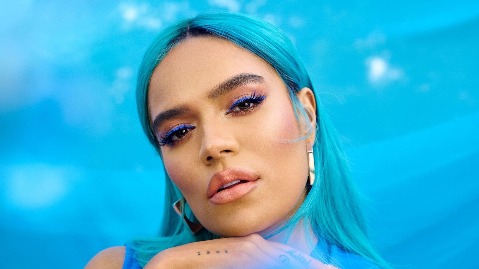 Karol G showing the barbed-wire heart tattoo on her arm