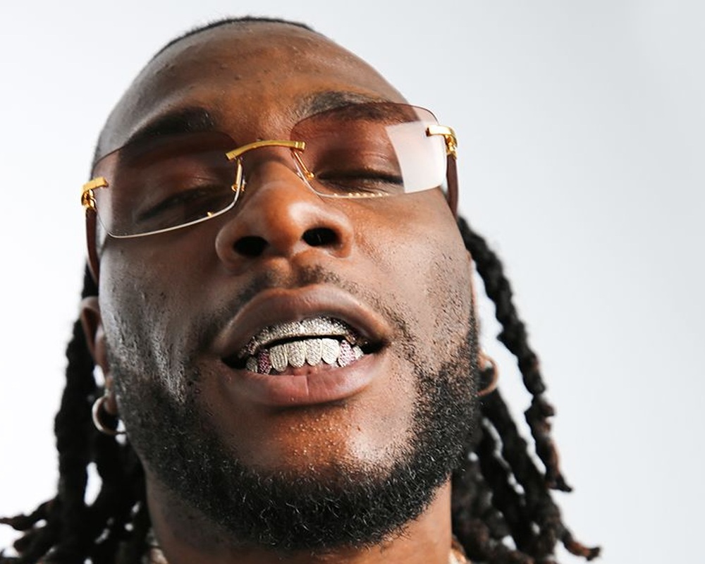 Burna Boy tattoos: Close tattoo-tour crop showing Burna Boy’s neck and upper-body lettering