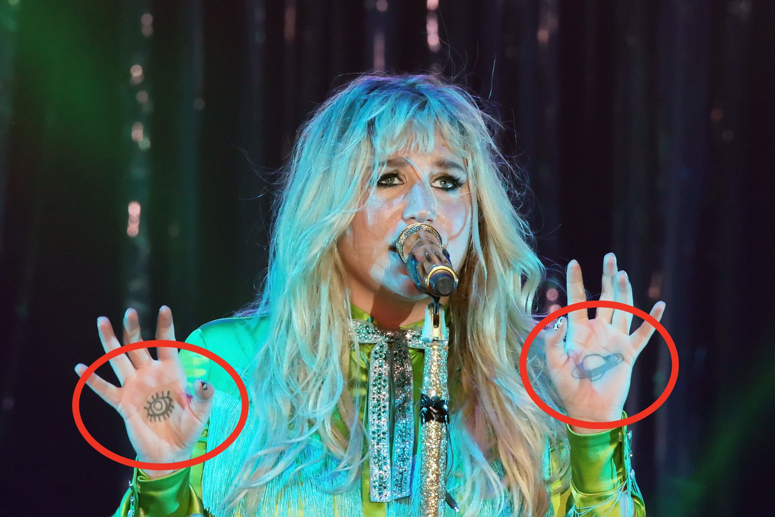 Kesha tattoos: Kesha's palm eye and Saturn hand tattoos visible in a stage photograph