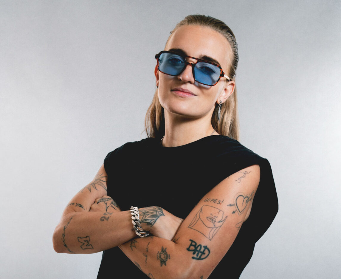 G Flip tattoos: separate arms-crossed portrait showing lettering and fine-line tattoos